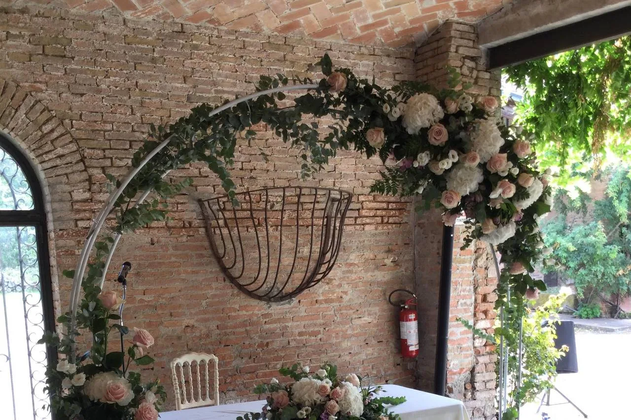 Arco di fiori e verde davanti a una parete di mattoni, allestimento per una cerimonia